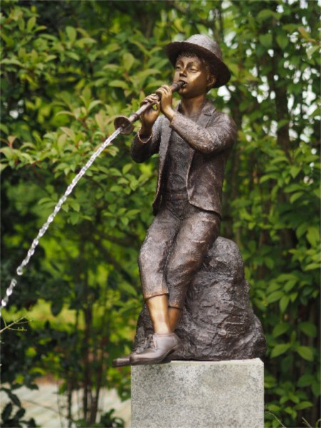 Jungen Tim sitzt auf einem Stein und spielt Flöte - Wasserspeier Bronzeskulptur